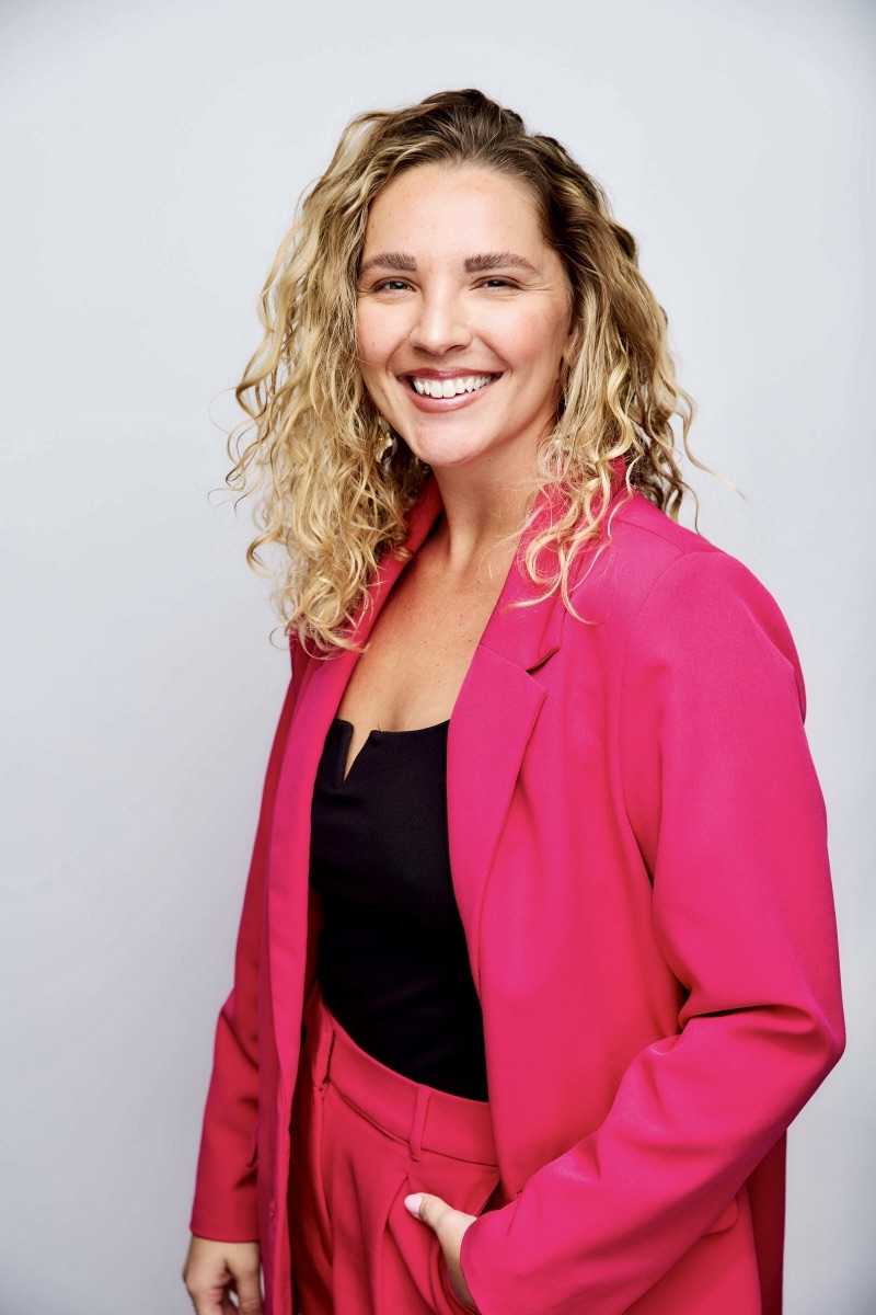 Portrait of Kiana Olmstead, smiling, in a bright pink blazer.